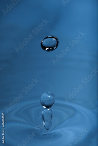 Drop falling into water on blue background, macro view © New Africa
