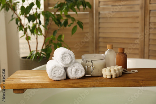 Wooden tray with spa products and towels on bath tub in bathroom