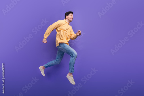 Full length photo of handsome young guy running energetic have fun wear trendy yellow garment isolated on violet color background © deagreez