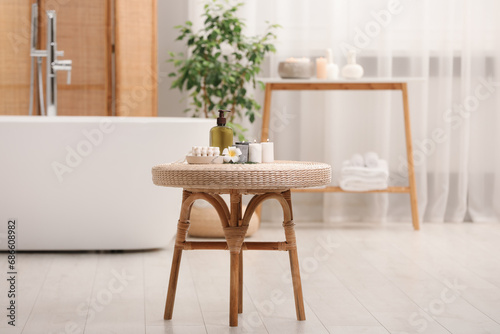 Spa products, burning candles and plumeria flower on small table in bathroom