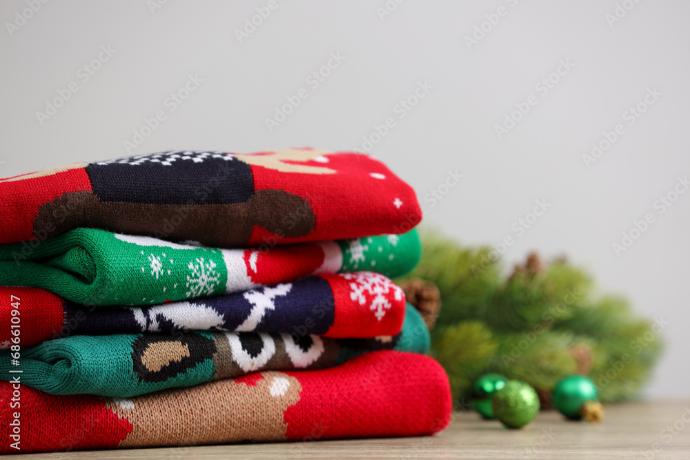 Stack of different Christmas sweaters, fir tree branch and baubles on table. Space for text