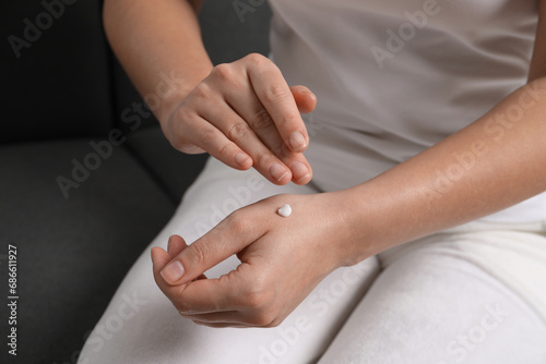 Woman applying cosmetic cream onto hand on sofa  closeup