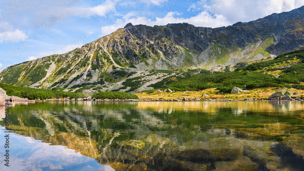 Polish Tatra Mountains, natural lake Przedni Staw Polski surrounded by high mountain peaks, view from the mountain hiking trail on a sunny summer day.