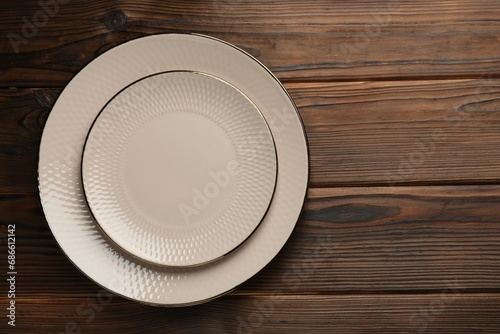 Beautiful beige ceramic plates on wooden table, top view. Space for text