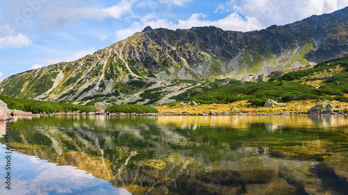 Polish Tatra Mountains, natural lake Przedni Staw Polski surrounded by high mountain peaks, view from the mountain hiking trail on a sunny summer day. © Castigatio