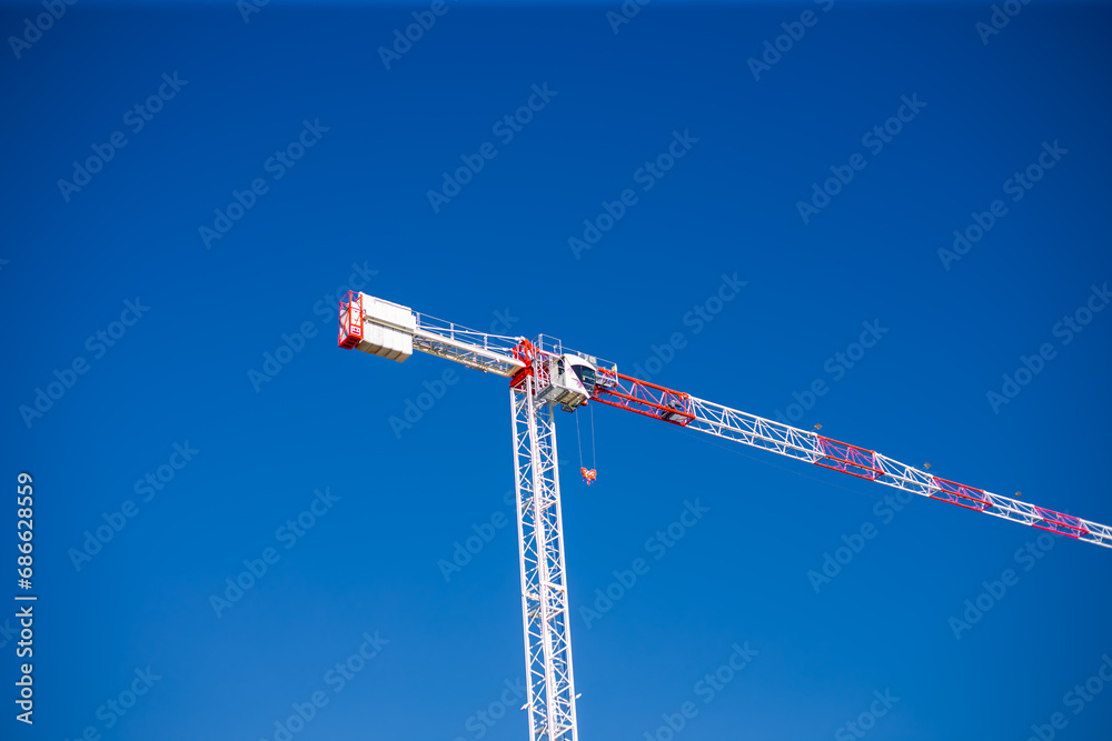 Construction cranes work on creation site against blue sky background. Bottom view of industrial crane. Concept of construction of apartment buildings and renovation of housing. Copy space Construction cranes work on creation site against blue sky background. Bottom view of industrial crane. Concept of construction of apartment buildings and renovation of housing. Copy space