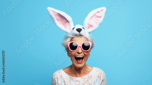 Old woman wearing bunnyears headband and goggles on isolated blue background - ai generative photo