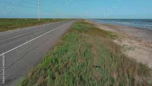 rThe road runs right along the seashore. Blue sky, sea, green grass, road, house on the beach. A bicycle and a car are driving along the road. Filming from a drone, road to the sea photo