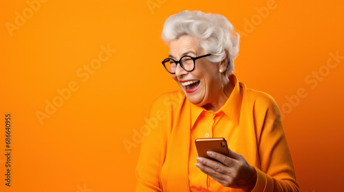 Happy senior woman waving on video call through smart phone against orange background © Olga