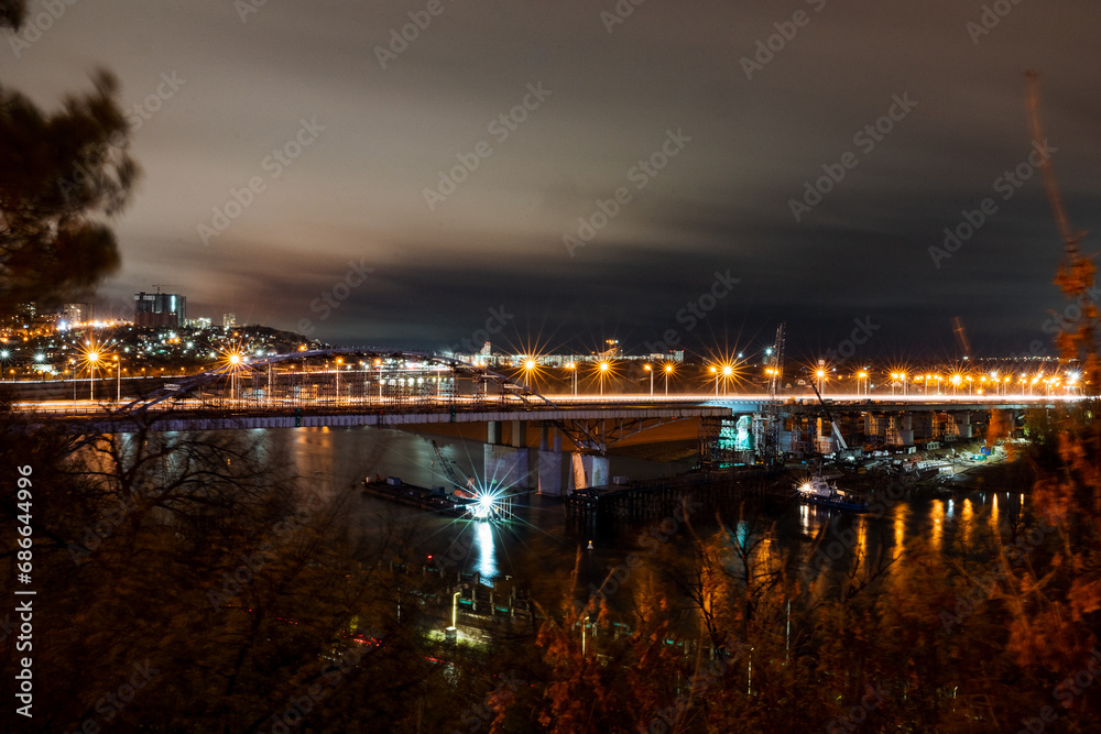 Night photo of a road bridge over a river, a cityscape. Lanterns of the night city.