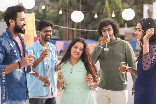 Groups of youthful friends with wine glasses in hand dancing together during birthday evening party - concept of festive celebration, entertainment and gathering photo