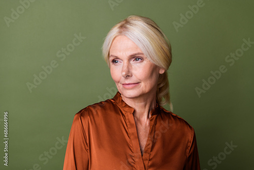 Photo portrait of attractive pensioner woman look thoughtful empty space wear trendy brown satin clothes isolated on khaki color background