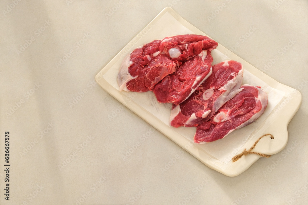 Lamb meat on a ceramic board on beige background. Meat for cooking. Rear part of the meat carcass. Top view.