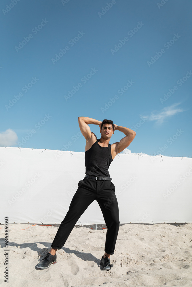 Strong and young cuban man in black outfit touching head and looking at camera in Miami, south beach Strong and young cuban man in black outfit touching head and looking at camera in Miami, south beach