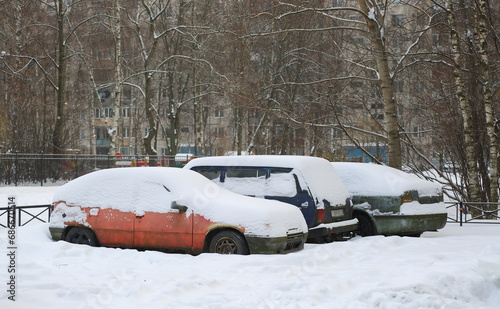 Snow-covered old cars in the parking lot in the courtyard of a residential building, Podvoysky Street, St. Petersburg, Russia, December 01 2023