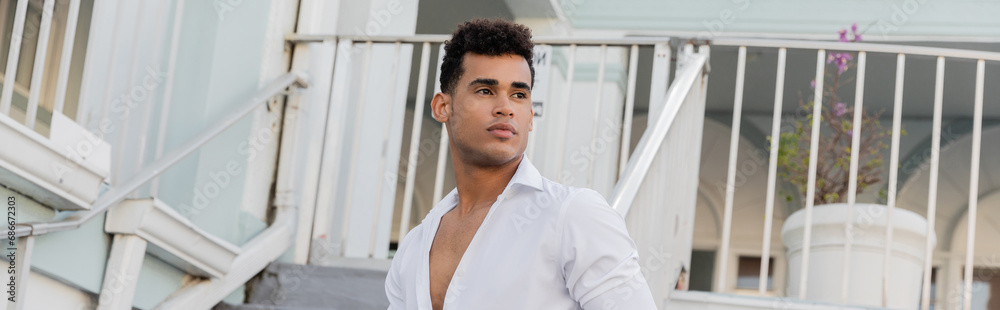 cuban man with curly hair and in white shirt looking away on urban street in Miami, banner cuban man with curly hair and in white shirt looking away on urban street in Miami, banner