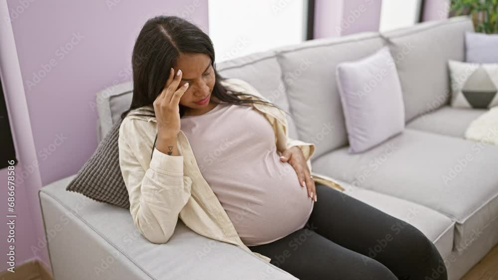 Young hispanic woman suffering a serious headache during pregnancy, sitting at home and massaging belly stressfully Young hispanic woman suffering a serious headache during pregnancy, sitting at home and massaging belly stressfully