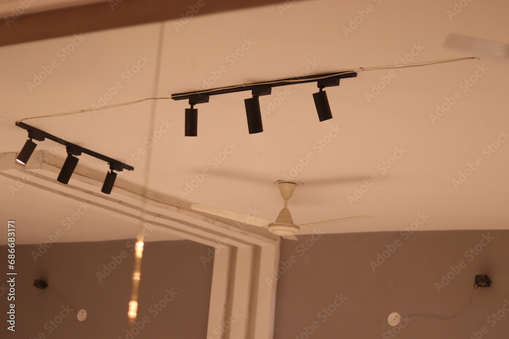 Mirror reflection of A ceiling fan and Two Black Aluminum Track Light illuminated by three Track spot light on the white ceiling Mirror reflection of A ceiling fan and Two Black Aluminum Track Light illuminated by three Track spot light on the white ceiling