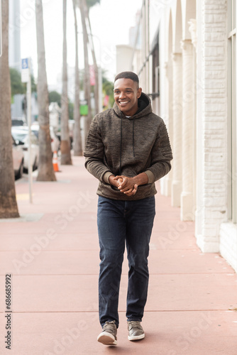 full length of cheerful african american man in hoodie and jeans walking on street in Miami