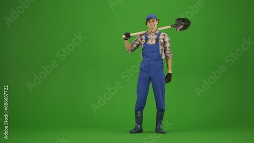 Portrait of farmer in working clothing on chroma key green screen. Gardener standing holding garden shovel on the shoulders.