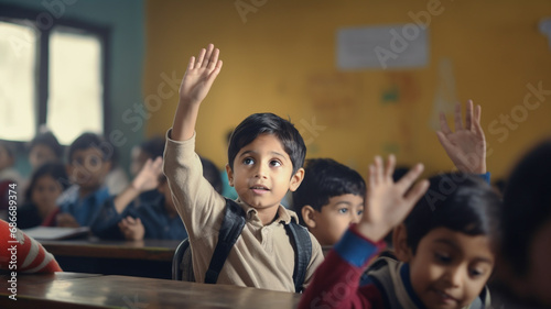 Small indian boy kid in school classroom raising hand up to answer teacher.

 photo