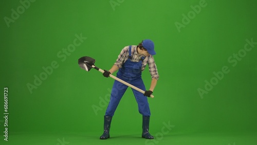 Portrait of farmer in working clothing on chroma key green screen. Gardener standing with shovel and hunting a mole.