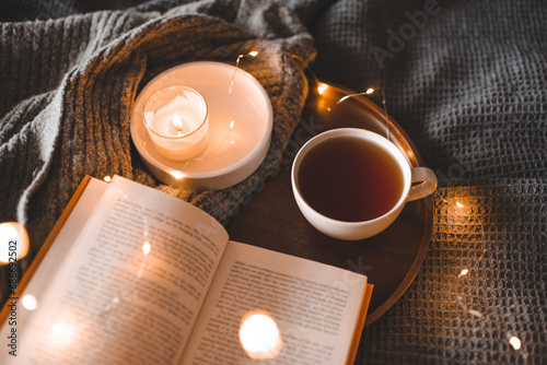 Obraz na plátně Cup of black tea with burning candle with open paper book on tray in bed over glowing Christmas lights close up