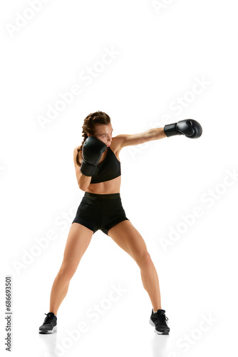 Striking image of female professional boxer in action, wearing gloves and shorts, standing out against plain white studio background.