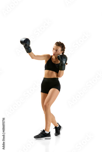 Fierce and confident, determined boxer girl, professional sportsman posing against white studio background. Concept of individual sport.