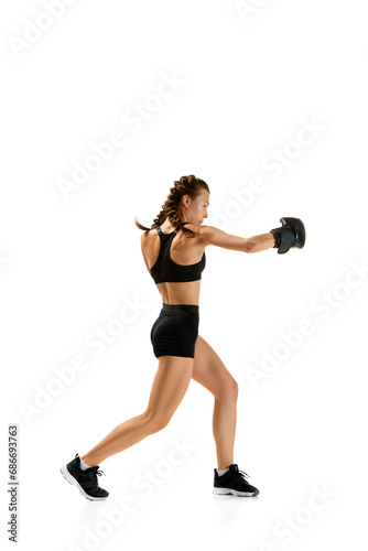Striking image of female, professional sportsman, boxer showcasing her prowess in boxing gear against clean white studio background.