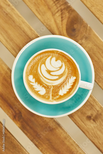 Top-down view of a beautifully crafted latte with art in a teal cup on a striped wood table