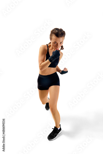 Powerful boxer girl in shorts and gloves striking pose against white studio background. Strength and competitiveness in sport.