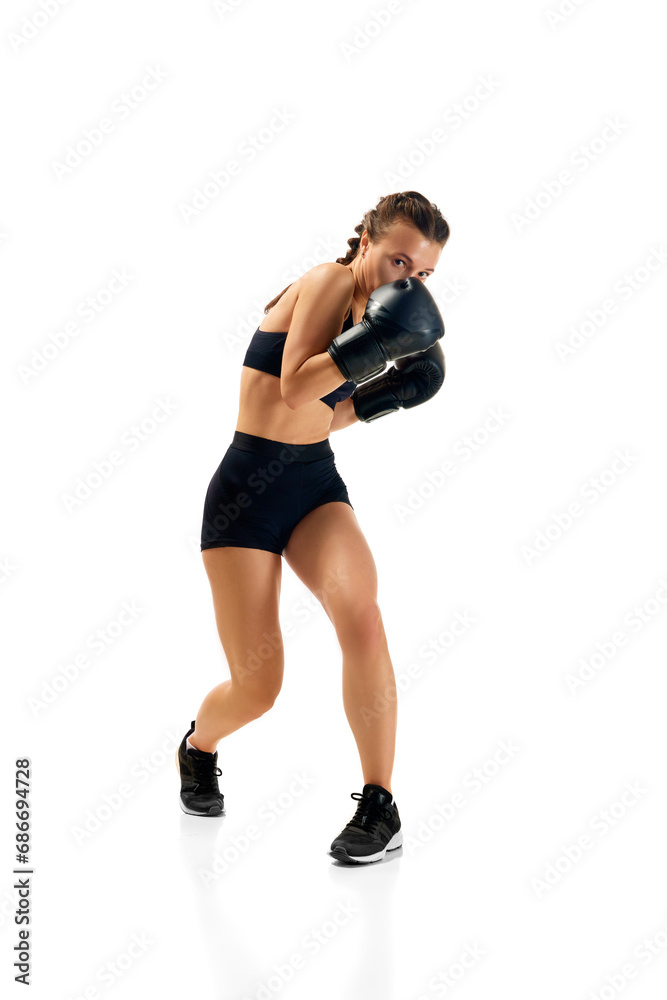 Dynamic portrait of sporty and powerful, young woman in boxing attire training in motion against white studio background. Concept of sport lifestyle, health.