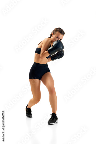 Dynamic portrait of sporty and powerful  young woman in boxing attire training in motion against white studio background. Concept of sport lifestyle  health.