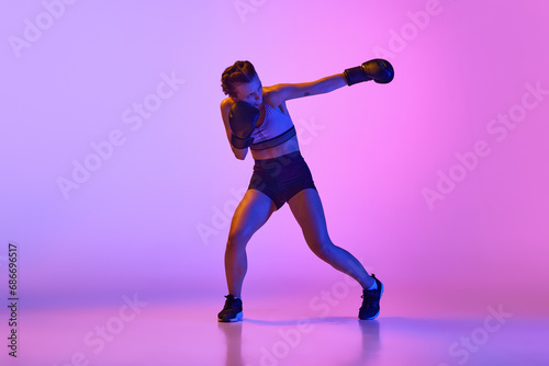 Dynamic and intense, female professional boxer showcases her athleticism against gradient violet studio background in neon light.