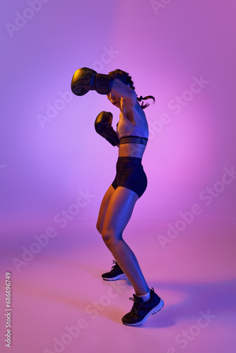 Fierce and confident  determined boxer girl  professional sportsman posing against gradient studio background in violet neon light. Concept of individual sport.