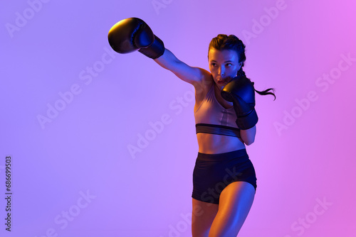Intense moment as determined boxer girl meticulously training, preparing for combat against gradient studio background in neon light.