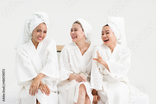 Three young Asian women in bathrobes, towels on heads, enjoy chatting. Female friends in gowns and towels have fun after spa in luxury hotel, wearing towels and bathrobes.