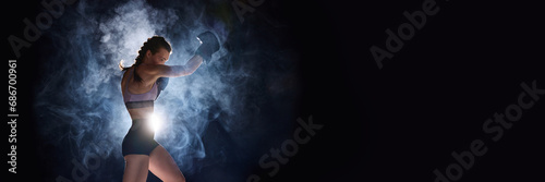 Banner. Flyer. Focused and powerful, female sportsman gearing up for battle, against black studio background in stage smoke. Negative space for text.