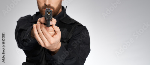 Looking down barrel of anonymous police officer's sidearm in studio. Crop view of unrecognizable constable aiming, by pointing handgun to camera, isolated on gray. Concept of danger, work, weapon. photo