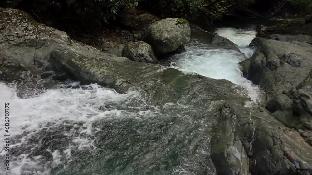 Waterfall cascade falling through stones and rocks in the woodland is filmed from above in slow motion. Tranquil scenery of forest river with strong stream and cliffs at summer. Relaxing view of creek