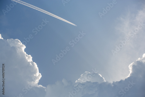 A high flying plane with a trail among epic white clouds and the blue sky. photo