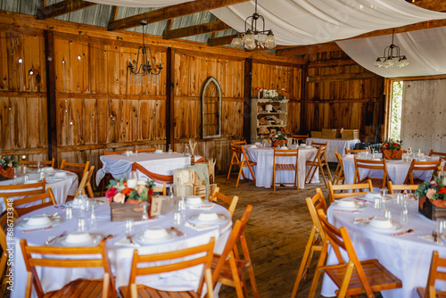 A wedding barn venue with decorated tables, fairy lights and draping chiffon hanging on top.
