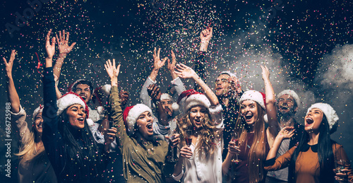 Joyful people throwing confetti while enjoying New Year atmosphere in night club with confetti flying around © gstockstudio