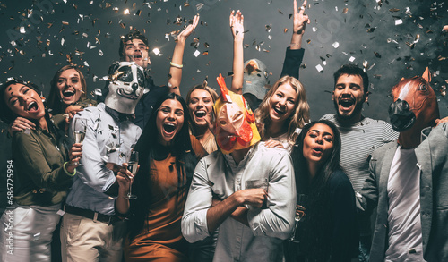 Group of happy young people in animal masks enjoying celebration in night club with confetti flying around