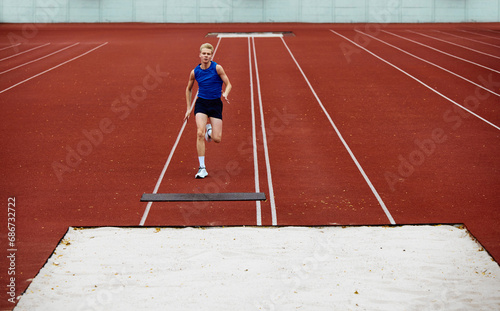 Approach. Focused runner propelling into sand pit. Young man, professional sportsman runner propelling into a sand pit.