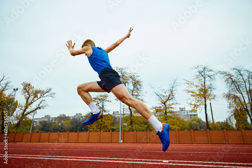 Dynamic steps leading to an impactful long jump. Bottom view full length portrait of professional sportsman running on sport field. photo