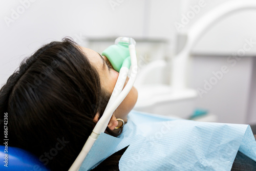 An adult woman sits in a dentist's clinic wearing a nasal mask to inhale nitrous oxide. Dentist fear concept. Feeling of relaxation with laughing gas. photo