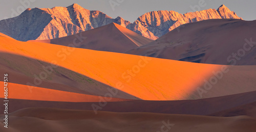 Sand dunes and the Naukluft Mountains in sunset golden glow in Namib-Naukluft Park; Sossusvlei, Namibia photo