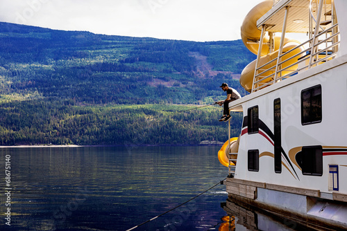 Man enjoying a family, houseboat vacation and fishing off of the deck of the houseboat while parked on the shoreline of Shuswap Lake; Shuswap Lake, British Columbia, Canada photo